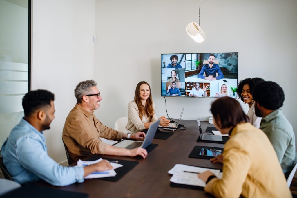 A group of people having a conversation in a conference room with a virtual meeting